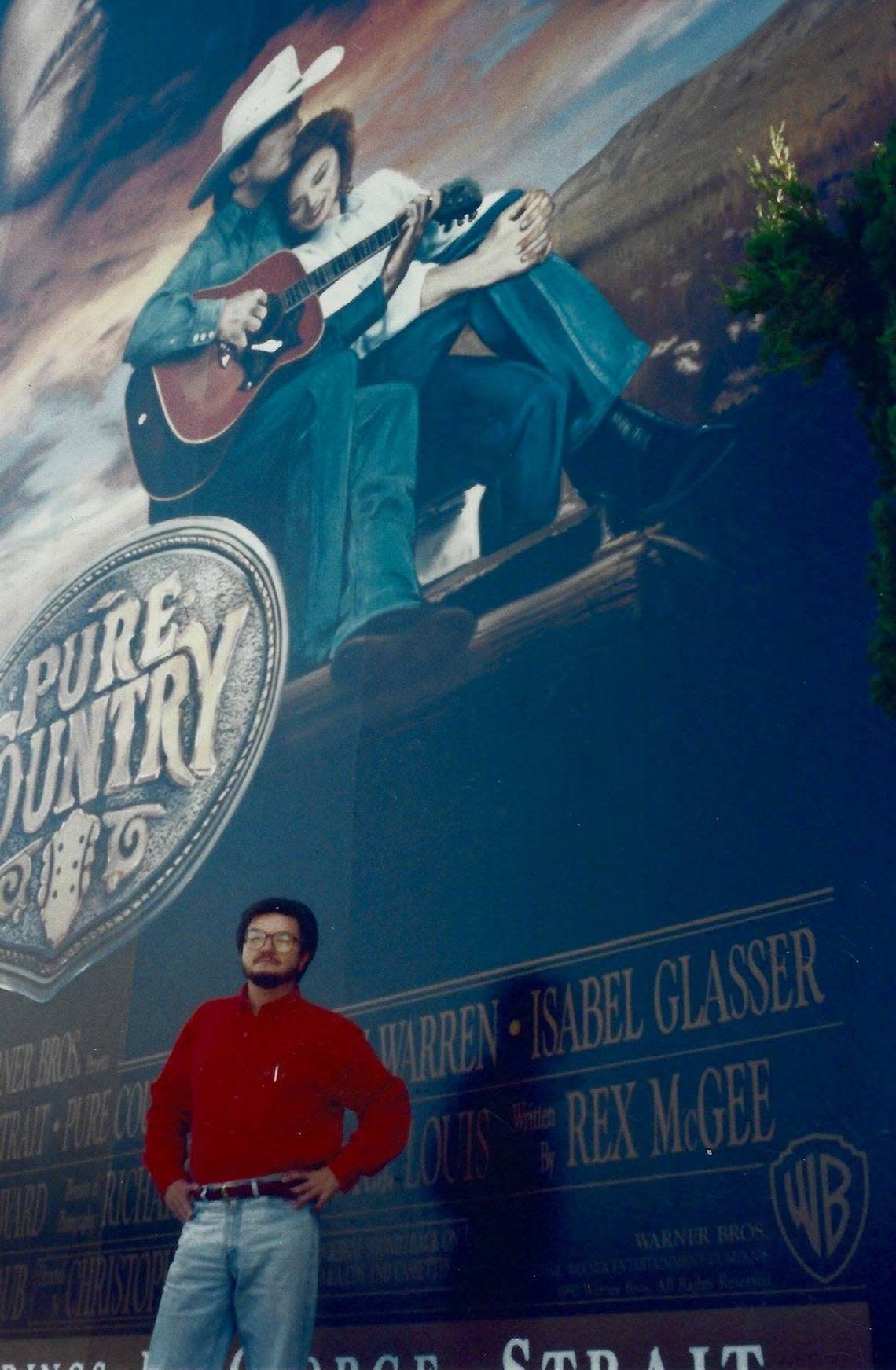 “Pure Country” screenwriter and North Texas native Rex McGee stands below a billboard of his movie.