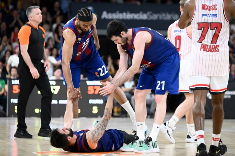 Ricky Rubio es ayudado a levantarse por sus compañeros del Barcelona Jabari Parkeer (izq.) y Álex Abrines (drcha.) tras la eliminación de su equipo en cuartos de final de la Euroliga de baloncesto ante el visitante Olympiakos el 8 de mayo de 2024 (Josep Lago)