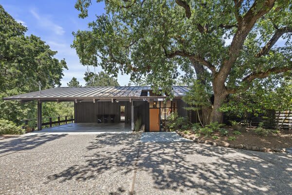 A wide paved drive leads to the remodeled home, where a bright orange door extends a cheerful welcome. Mature oak, pine, and bay trees encompass the private half-acre lot.