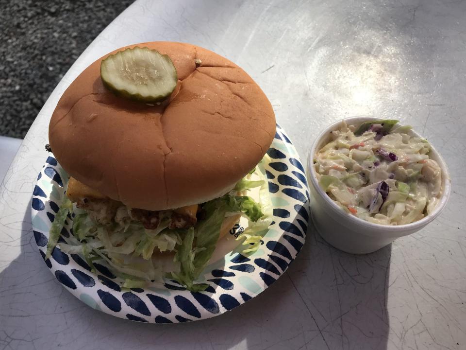 Halibut burger on a paper plate beside side of coleslaw from arctic roadrunner in alaska