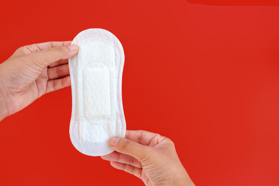 Cropped Hands Holding White Sanitary Pad Against Red Background