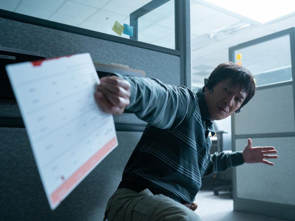 ke huy quan in everything everywhere all at once. he's crouched down near a cubicle wall, having caught a document behind him, and wearing earpieces