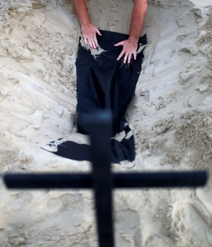 An activist of the NGO Rio de Paz places a black blanket inside one of the one hundred graves which were dug on Copacabana beach, symbolising the dead from the coronavirus disease (COVID-19), during a demonstration in Rio de Janeiro