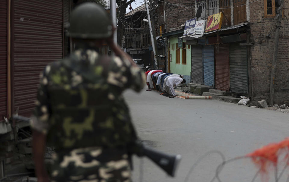 An Indian paramilitary soldier stands guard as Kashmiri Muslims offer Friday prayers on a street outside a local mosque during curfew like restrictions in Srinagar, India, Friday, Aug. 16, 2019. India's government assured the Supreme Court on Friday that the situation in disputed Kashmir is being reviewed daily and unprecedented security restrictions will be removed over the next few days, an attorney said after the court heard challenges to India's moves. (AP Photo/Mukhtar Khan)