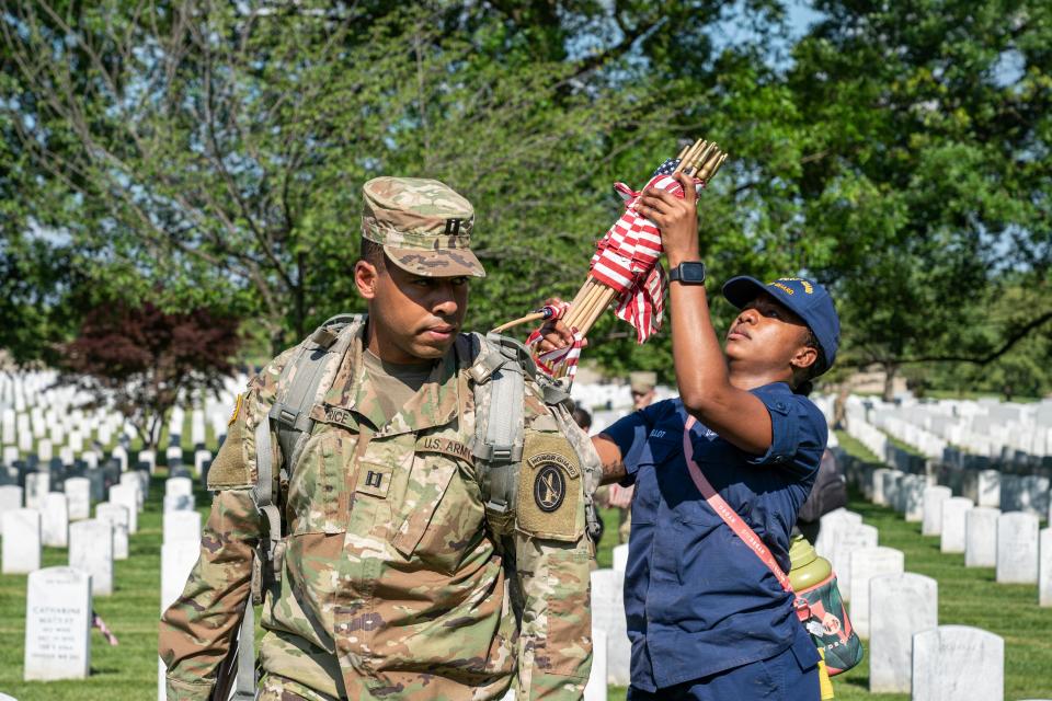 Captain Benjamin Grice turns so Seaman SN Bellot can grab more flags while members of the 3rd United States Infantry Regiment, also known as The Old Guard, place flags in front of each headstone as part of the "Flags In" ceremony at Arlington National Cemetery in Arlington, Va. on Thursday, May 27, 2021.