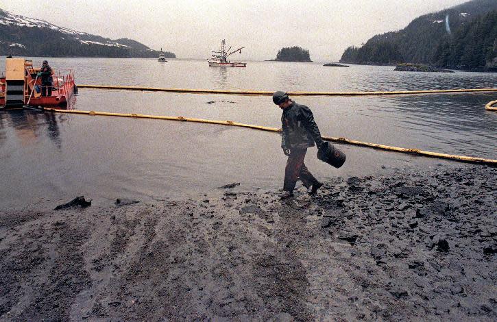 FILE - In this April 17, 1989, file photo, a worker makes his way across the polluted shore of Block Island, Alaska, as efforts are underway to test techniques to clean up the oil spill of the tanker Exxon Valdez in Prince William Sound. The worker periodically uses the bucket to scoop up oil washing back onto shore from the containment booms. Nearly 25 years after the Exxon Valdez oil spill off the coast of Alaska, some damage heals, some effects linger in Prince William Sound. (AP Photo/John Gaps III, File)