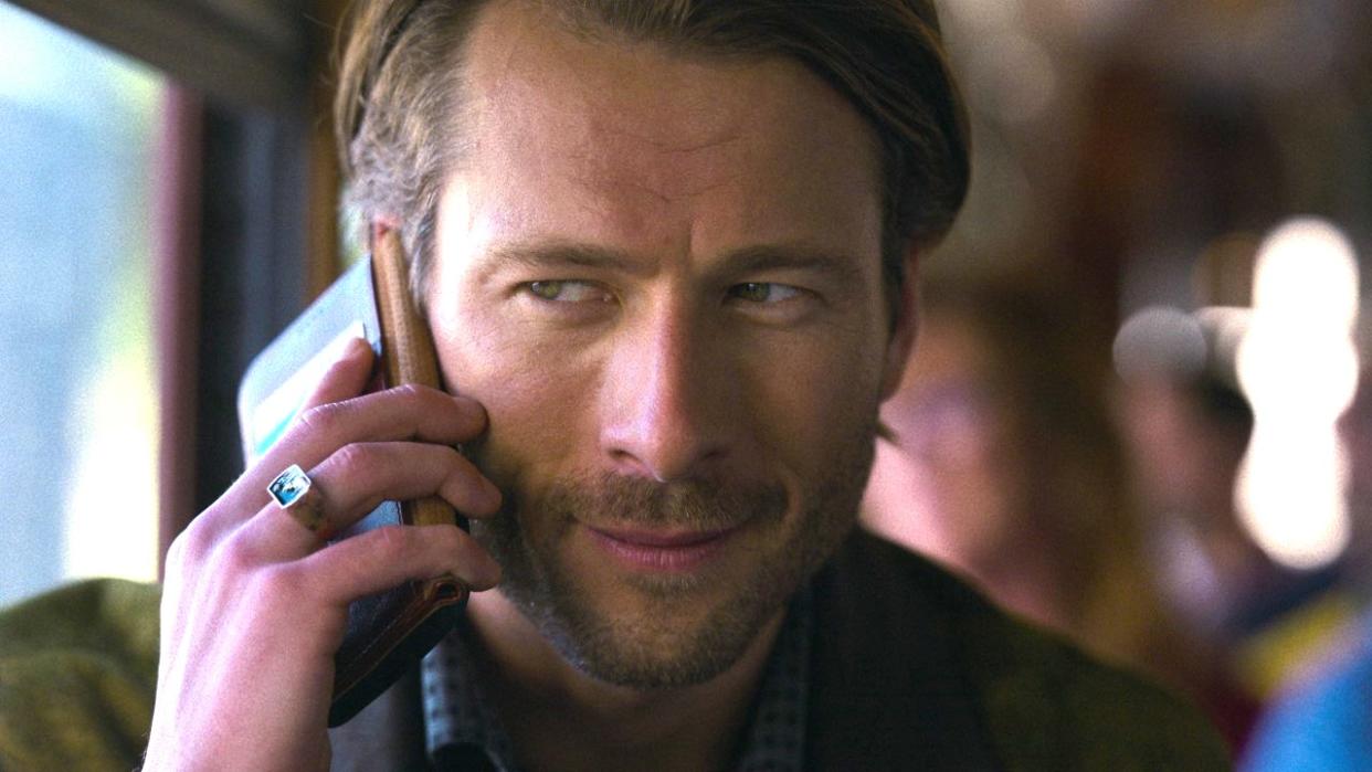  Glen Powell's Gary Johnson speaks on a phone in a close-up photo of his face in a press image for the Netflix movie Hit Man. 