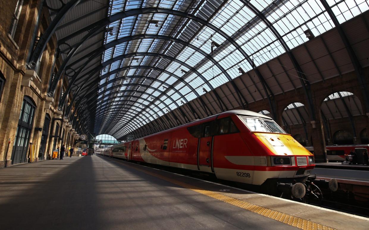 A long train in red-and-white LNER livery waiting at an almost-empty platform in the great train shed at Kings Cross