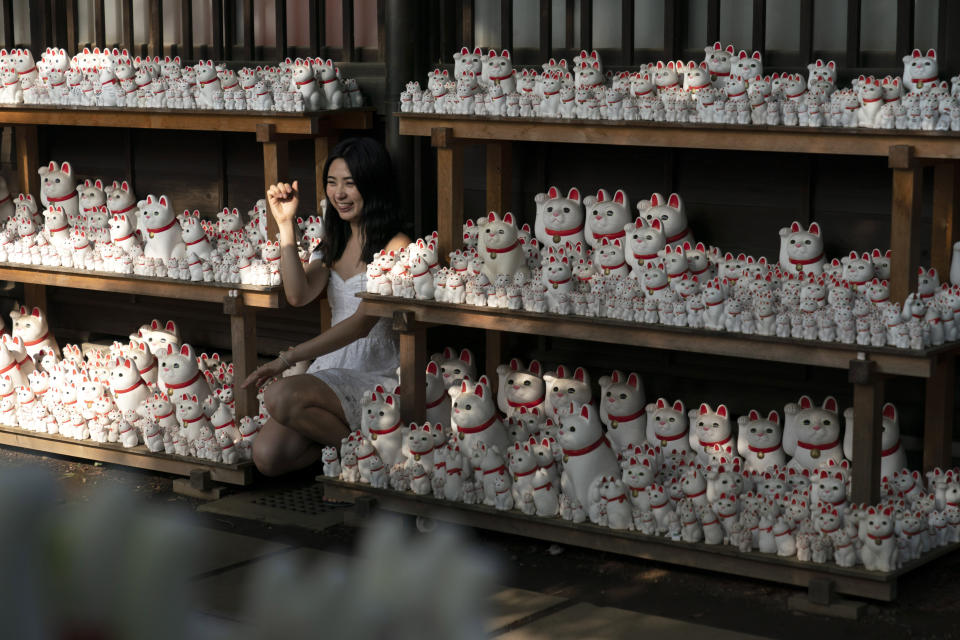 In this June 25, 2019, photo, a woman poses for photos with beckoning cat figurines at Gotokuji Temple in Tokyo. According to a centuries-old legend provided by the temple, Gotokuji, a Buddhist temple located in the quiet neighborhood of Setagaya, is the birthplace of beckoning cats, the famous cat figurines that are widely believed to bring good luck and prosperity to home and businesses. Some visitors come just to snap a few photos, while others make a trip to the temple to pray and make wishes. (AP Photo/Jae C. Hong)