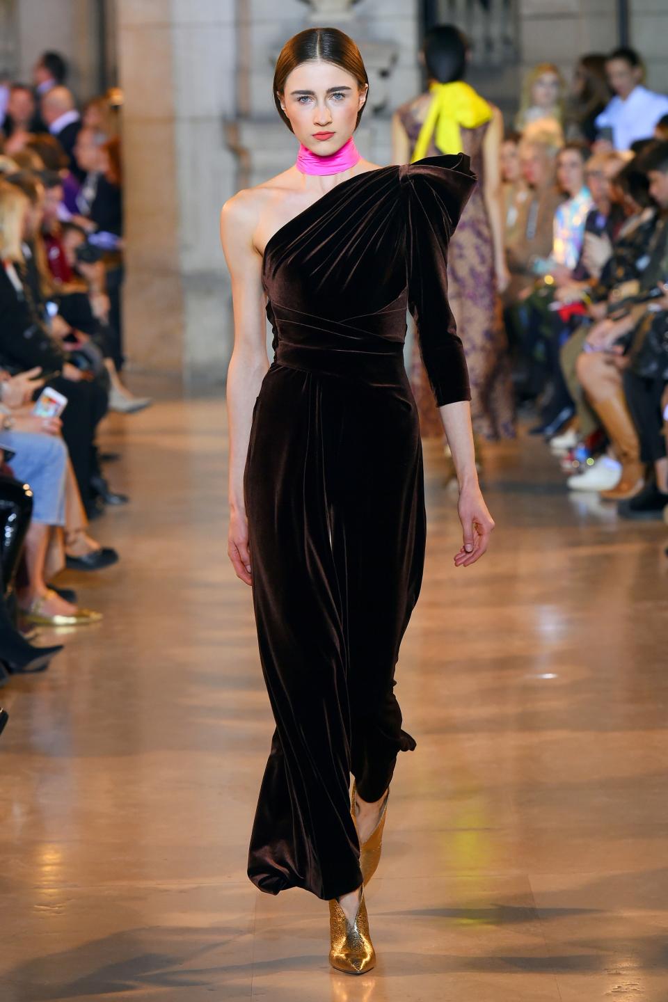 <p>Der One-Shoulder-Jumpsuit aus Samt beeindruckt mit einer femininen Silhouette, die vor allem durch die schmale Taille in Wickeloptik zustande kommt. Farbliches Highlight an dem Look sind ein Choker in Pink und goldene Stiefeletten. (Bild: Talbot Runhof) </p>