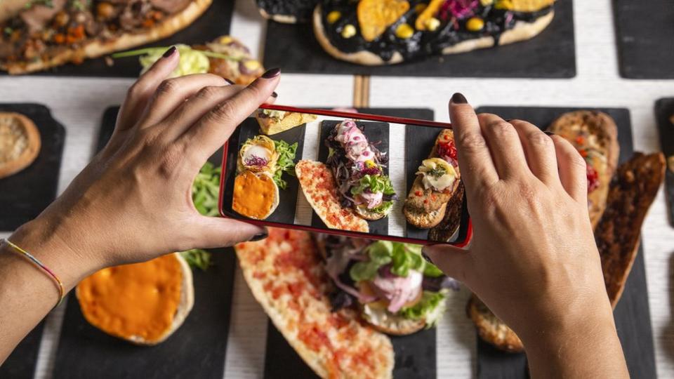 Una mujer fotografiando distintos platos de comida con su teléfono