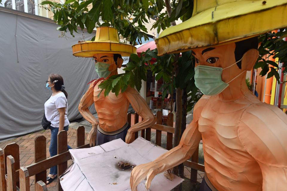 A woman walks past a display of two cultural figurines of men wearing masks in Singapore on 12 June, 2020. (PHOTO: AFP via Getty Images)