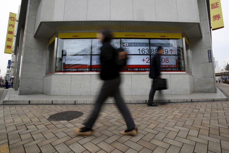 FILE PHOTO: Pedestrians walk pass an electronic board outside a brokerage in Tokyo