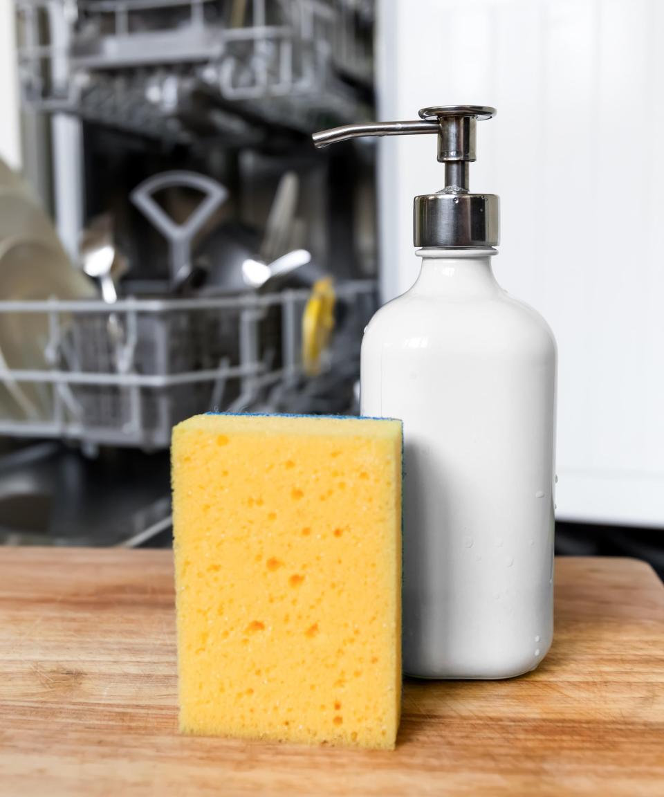 A bottle of dish soap and a sponge in front of a dishwasher