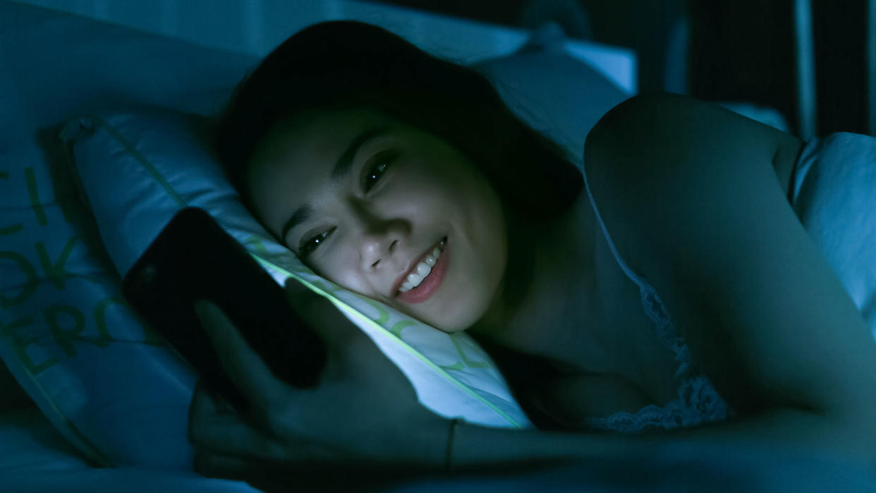 Stock image of woman looking at her phone at night in bed. (Photo: Getty Images)