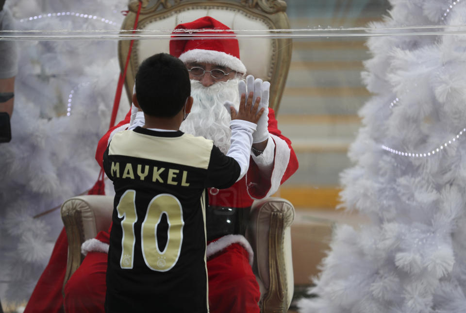 Dressed as Santa Claus, David Pizarro, talks with a boy from inside a plastic enclosure in an effort to curb the spread of COVID-19, at a square in the Comas municipality of Lima, Peru, Monday, Dec. 21, 2020. (AP Photo/Martin Mejia)