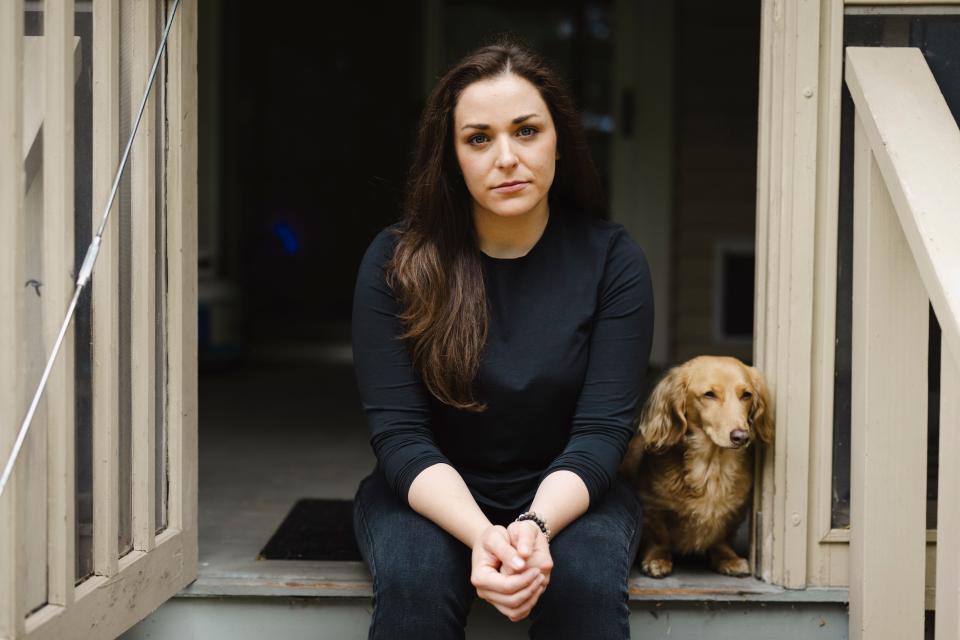 A woman with long brown hair sits on a porch with her dog