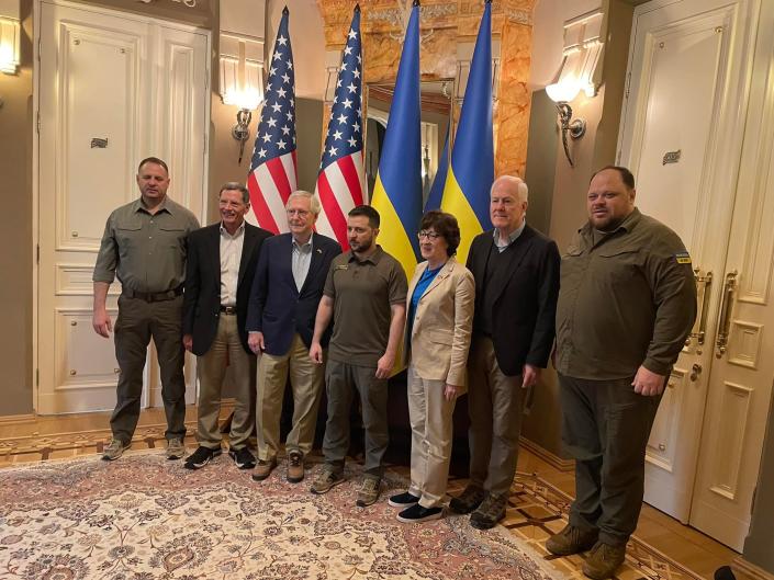 President Volodymyr Zelensky stands with Republican leaders in a carpeted state room in front of two American and two Ukrainian flags, with two Ukrainians in military drab at either end of the lineup...