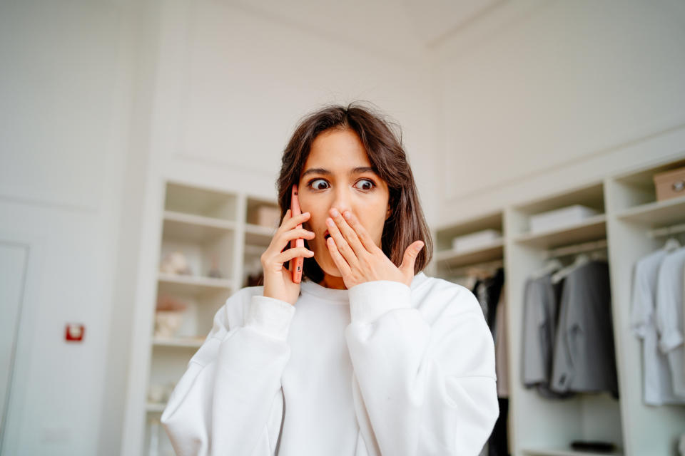 Person in a white sweatshirt looking surprised with hands covering mouth