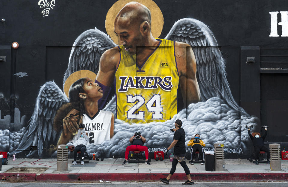 People lift weights on a sidewalk outside the Hardcore Fitness gym, due to COVID-19 restrictions, under a mural honoring NBA star Kobe Bryant and his daughter Gigi near Staples Center in downtown Los Angeles, Monday, Jan. 25, 2021. Bryant, who became one of the greatest basketball players of his generation during a 20-year career with the Lakers, died in a helicopter crash with his daughter Gigi and other passengers on Sunday, Jan. 26, 2020. (AP Photo/Damian Dovarganes)