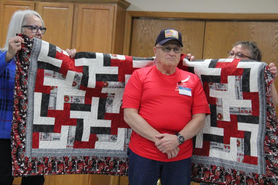 Members of the Perry Piecemakers help wrap Jim Cornelius in a Quilt of Valor during a presentation on on Friday, Nov. 10, 2023, at the Perry Elks Lodge.