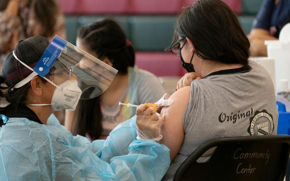 Sisters Guadalupe Flores, 15, right, and Estela Flores, 13, left, from East Los Angeles, get vaccinated with the Pfizer's COVID-19 vaccine by licensed vocational nurse Rita Orozco, far left, at the Esteban E. Torres High School in Los Angeles, Thursday, May 27, 2021. Vaccinated Californians will be eligible for $116.5 million in prize money. - AP