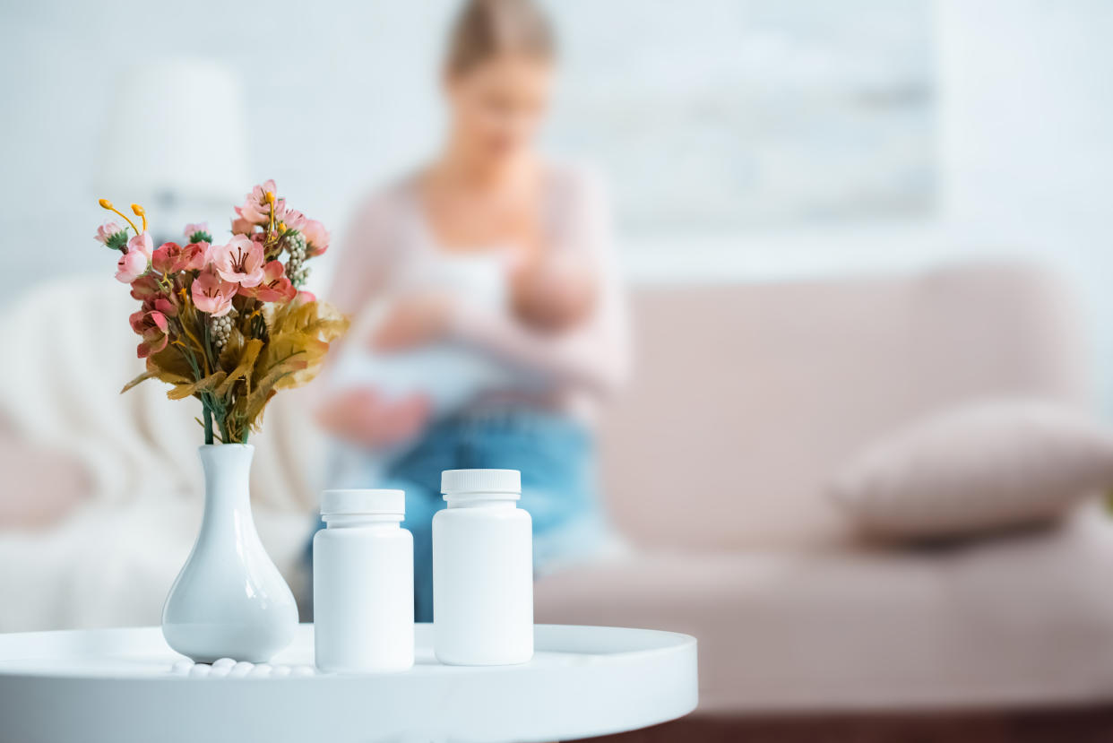 blurred woman breastfeeding baby with white pill bottles and vase of flowers in forefront, breastfeeding drug domperidone, psychological concerns 