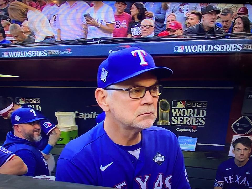 Michael Lacey, wearing dark glasses and a blue shirt, sits in the front row behind the Texas Rangers dugout during Game 5 of the 2023 World Series at Chase Field on Nov 1, 2023. This screenshot was taken from the World Series television broadcast.