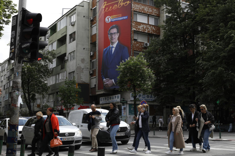 People cross a street where an election poster of Stevo Pendarovski, incumbent President and a presidential candidate backed by the ruling social democrats (SDSM), hangs on a building in Skopje, North Macedonia, on Monday April 22, 2024. Voters go to the polls in North Macedonia on Wednesday April 24 for the first round of presidential elections, the seventh such election since the Balkan country gained independence from the former Yugoslavia in 1991, where seven candidates are vying for the largely ceremonial position. (AP Photo/Boris Grdanoski)