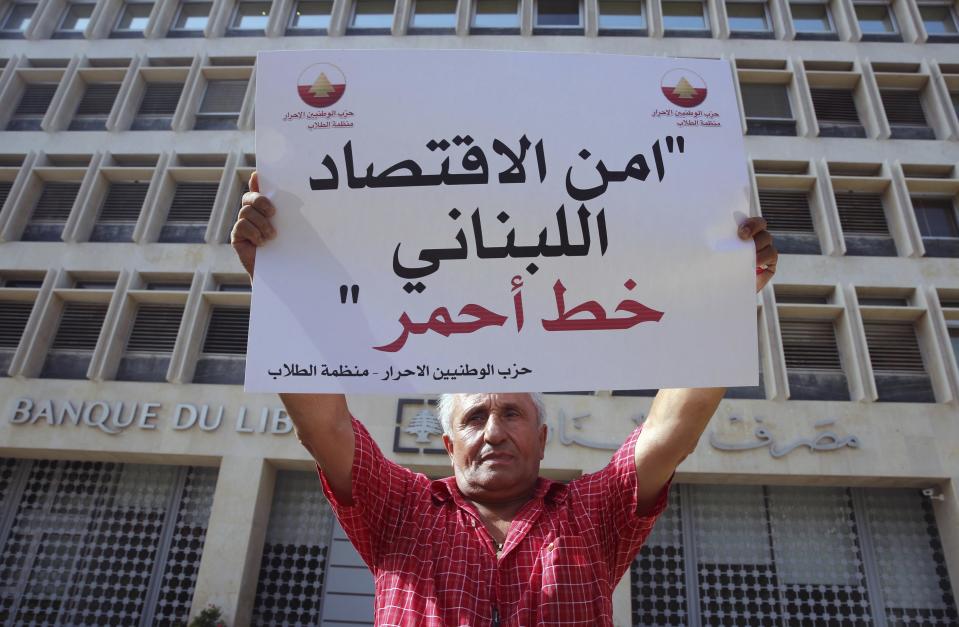 FILE - In this June 14, 2016 file photo, a Lebanese man holds a placard in Arabic thats reads"the security of Lebanon's economy is a red line," during a sit-in organized by anti-Syrian groups in front of the Lebanese Central Bank to show their solidarity with the Lebanese banks after a bomb exploded at Blom Bank headquarters on Sunday evening, in Beirut, Lebanon. In Syria nowadays, there is an impending fear that all doors are closing. After nearly a decade of war, the country is crumbling under the weight of years-long western sanctions, government corruption and infighting, a pandemic and an economic downslide made worse by the financial crisis in Lebanon, Syria's main link with the outside world. (AP Photo/Bilal Hussein, File)