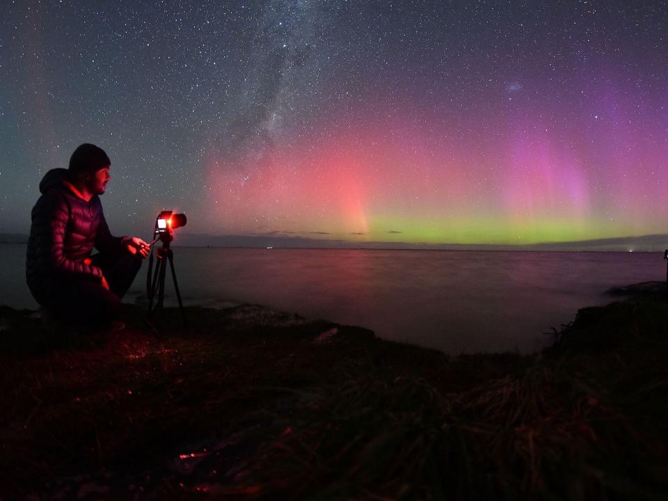 A man in heavy clothing takes pictures of the southern lights.