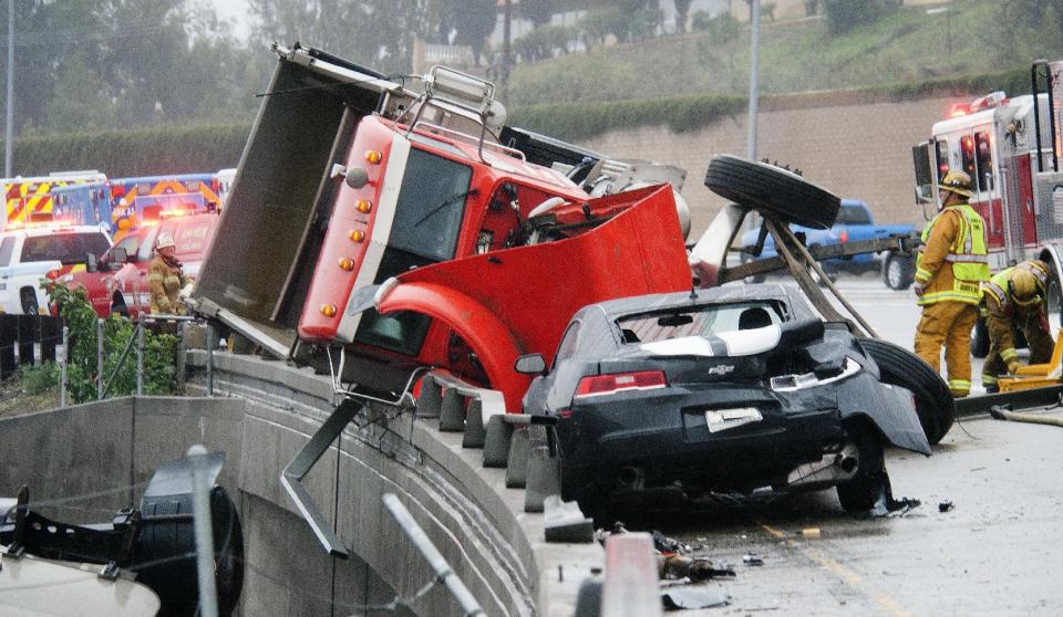 A Chevrolet Camaro stopped short of crashing into a partially overturned two-trailer dirt-hauling dump truck after it's driver slid, tipped and wound up partially dangling off the ramp from the eastbound 91 freeway to the northbound 55 Friday, Dec. 16, 2016, in Anaheim, Calif. A late fall storm has drenched California, causing some mud flows, roadway flooding and traffic snarls as it takes parting shots at the south end of the state. (Ken Steinhardt/The Orange County Register via AP)
