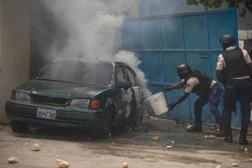 A police officer throws water on a burning vehicle in the parking area of the police headquarters during a protest to demand the resignation of Prime Minister Ariel Henry in the Petion-Ville area of Port-au-Prince, Haiti, Monday, Oct. 3, 2022.