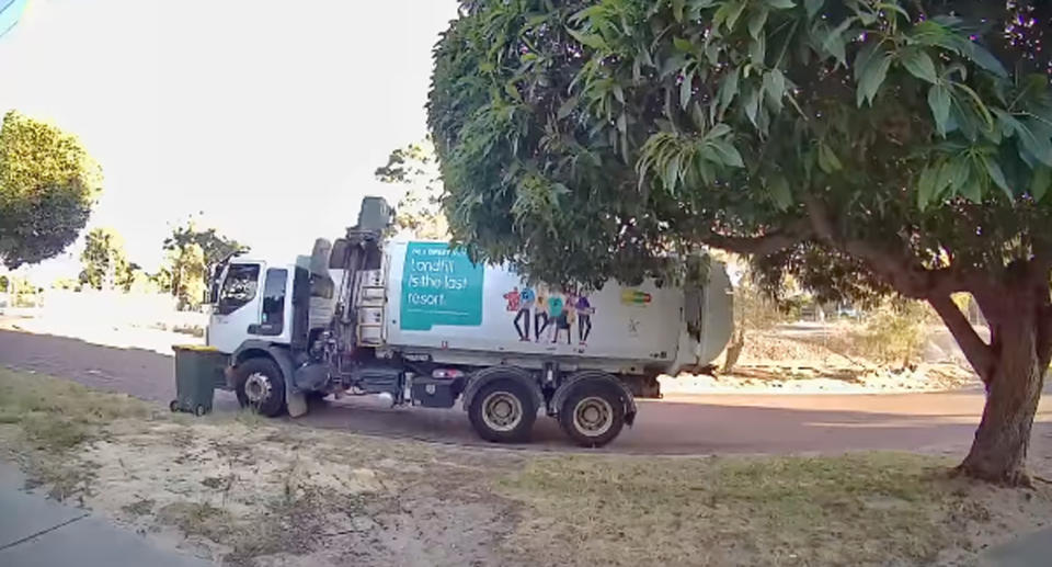 Garbage truck collecting wheelie bin on side of suburban street. 