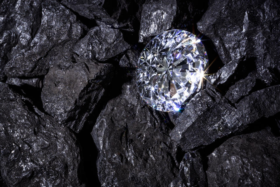 A single solitaire Diamond in amongst some pieces of coal.