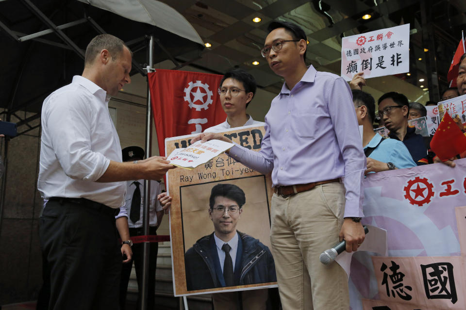 In this Thursday, May 23, 2019, photo, pro-China protesters hold a picture of Hong Kong activist Ray Wong Toi-yeung as they hands a letter to a representative from German Consulate General, left, in Hong Kong to against Germany in granting refugee status for the Hong Kong activists. Hong Kong's leader has summoned the German consul to complain over Germany granting political asylum to a pair of Hong Kong political activists. Carrie Lam on Friday called the pair bail jumpers who were facing charges including rioting and assaulting police over a violent incident in Feb. 2016. (AP Photo/Kin Cheung)