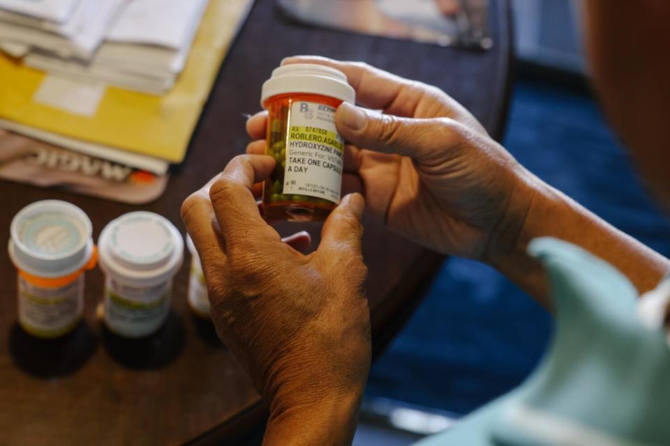 A pair of hands holding a bottle of prescription pills, with other bottles on a table