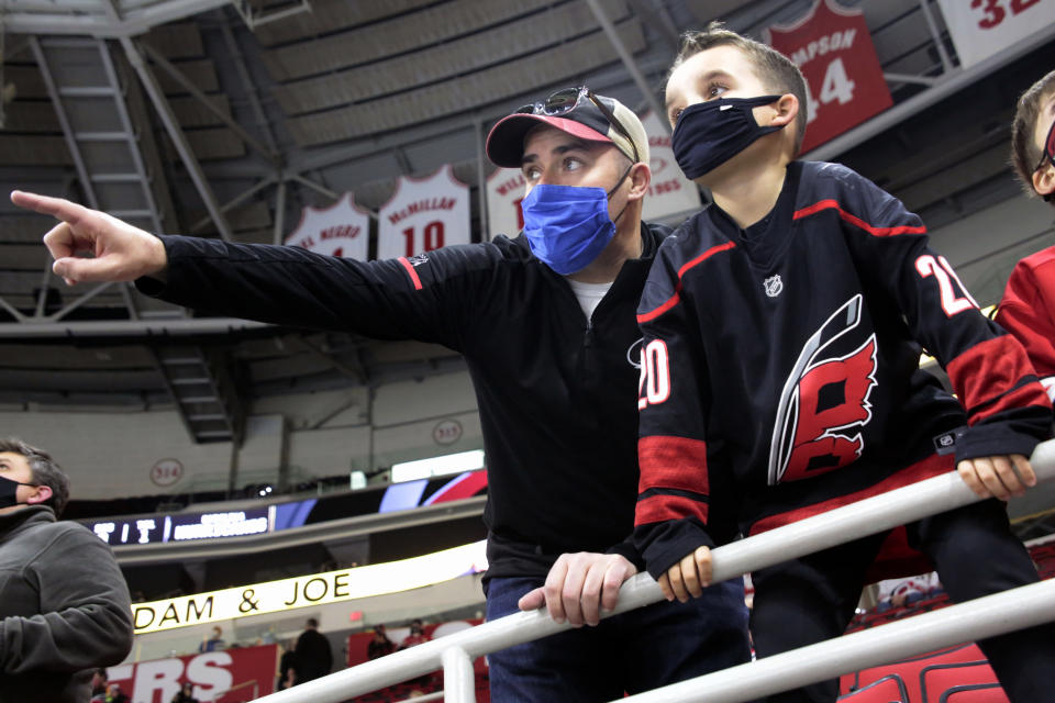 Derek DeYoung, left, points out players to his son Dominic DeYoung as the Carolina Hurricanes warm up before an NHL hockey game against the Detroit Red Wings in Raleigh, N.C., on Thursday, March 4, 2021. It is the first game where a limited number of fans have been allowed in PNC Arena to watch the team. (AP Photo/Chris Seward)