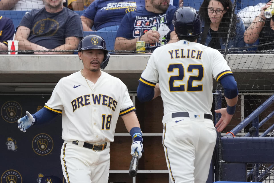 Milwaukee Brewers' Christian Yelich (22) returns to the dugout and greetings from Keston Hiura after scoring against the Cincinnati Reds during the first inning of a spring training baseball game Sunday, March 19, 2023, in Phoenix. (AP Photo/Ross D. Franklin)