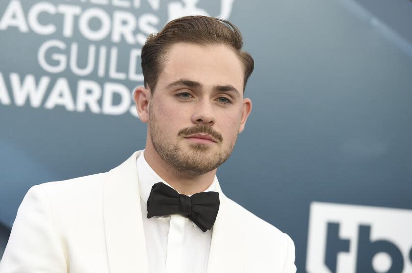 Dacre Montgomery in a white tuxedo jacket and dress shirt with a black bow-tie