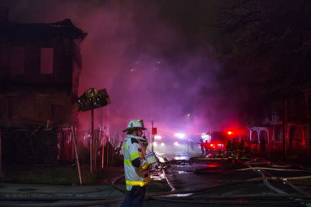 A Baltimore city firefighter walks past smoke, which was lit red from nearby fire engines, while battling a blaze at a residence in west Baltimore April 28, 2015. REUTERS/Adrees Latif