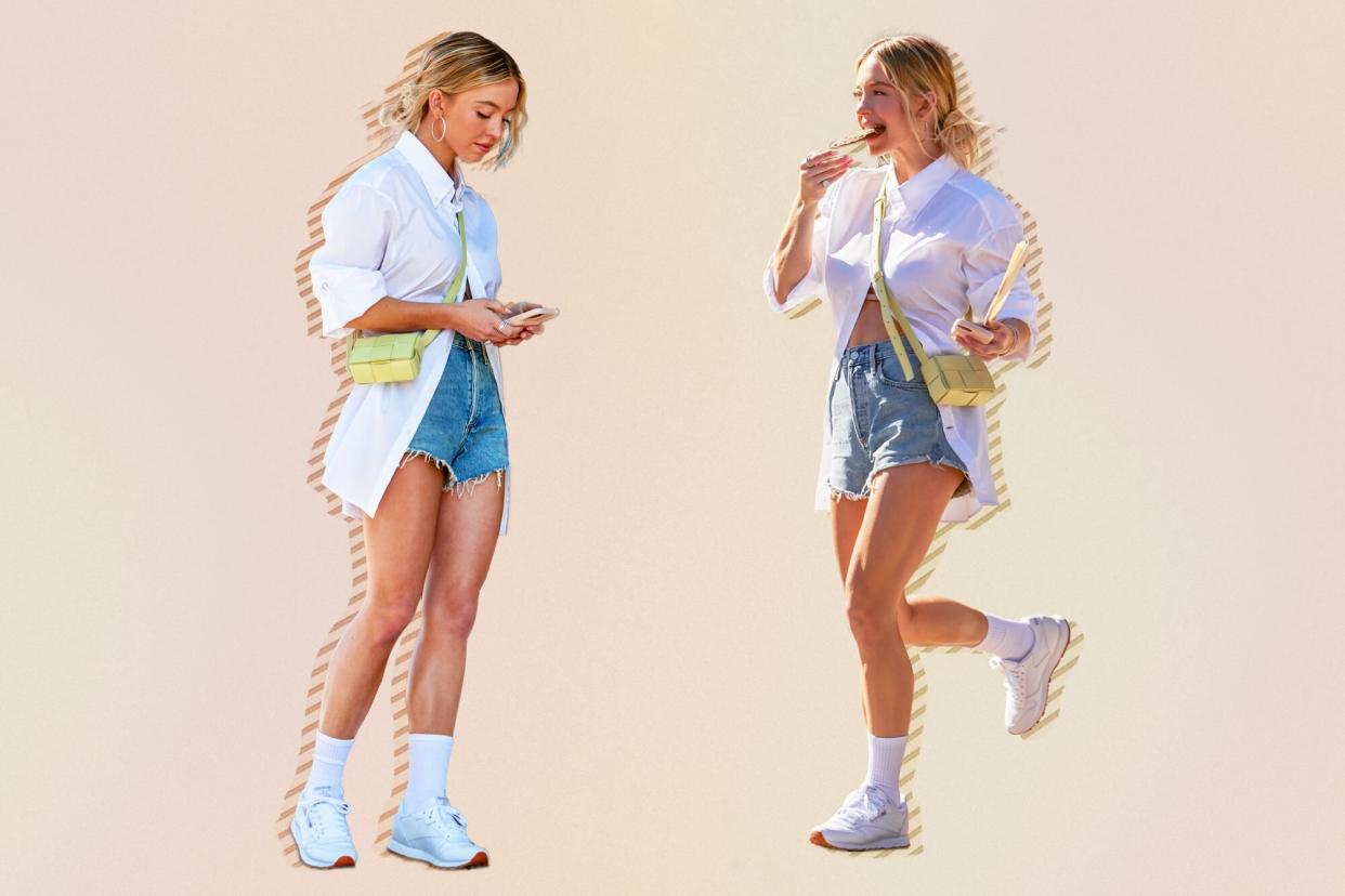 Sydney Sweeney wearing a white button down, jean shorts, and white reebok sneakers on a beige background