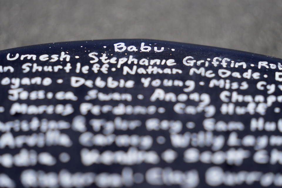 A surfboard belonging to Dan Fischer, of Newport, R.I., features the nickname of his late father "Babu," top, above the names of other families' lost loved ones, at Easton's Beach, in Newport, Wednesday, May 18, 2022. Fischer, 42, created the One Last Wave Project in January 2022 to use the healing power of the ocean to help families coping with a loss, as it helped him following the death of his father. Fischer places names onto his surfboards, then takes the surfboards out into the ocean as a way to memorialize the loved ones in a place that was meaningful to them. (AP Photo/Steven Senne)