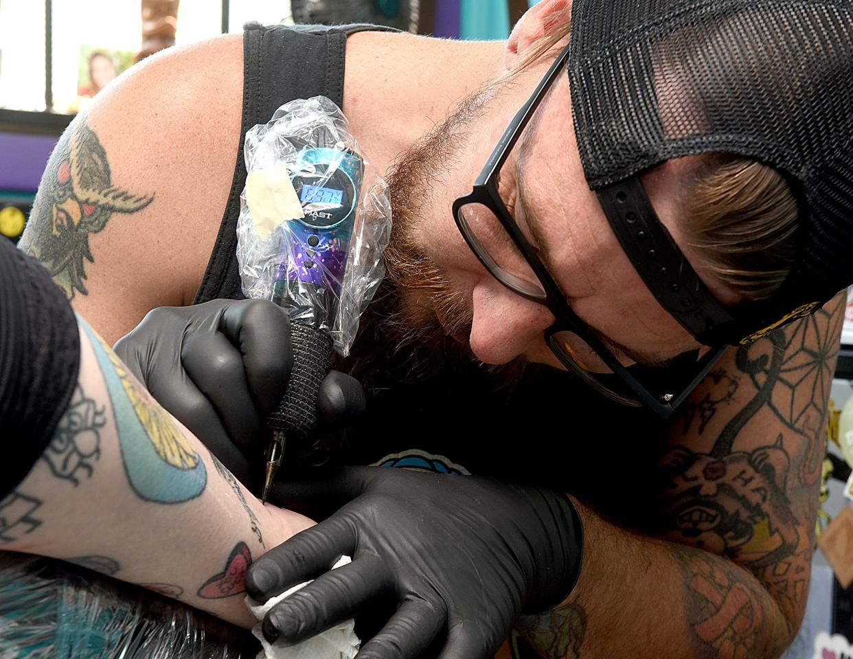 Megan Bedford relaxes as Tyler Hague, owner of The Electric Peacock, tattoos a frog holding a wine glass on her ankle on Thursday.