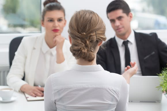 A woman sits across from a man and a woman at a job interview.