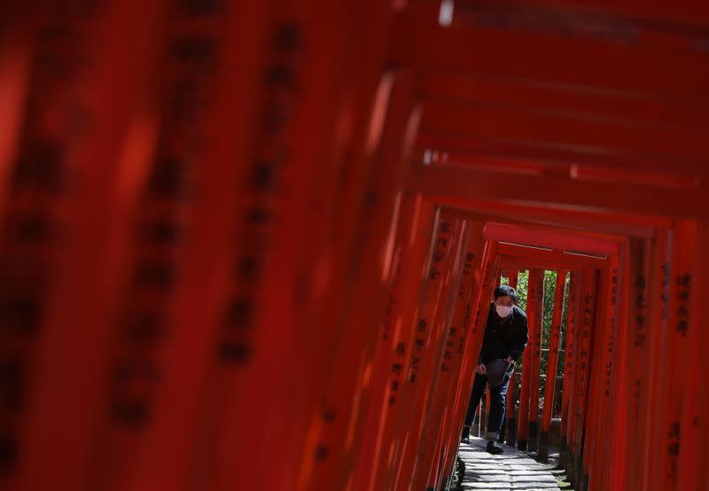 Man wearing protective face mask walks through red-coloured wooden torii gates at the Nezu shrine in Tokyo