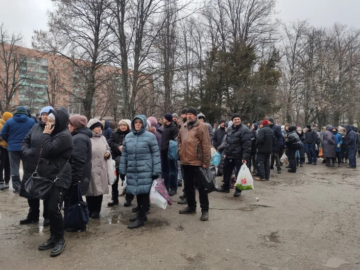 Dozens of people line up outside a hospital to receive food. 