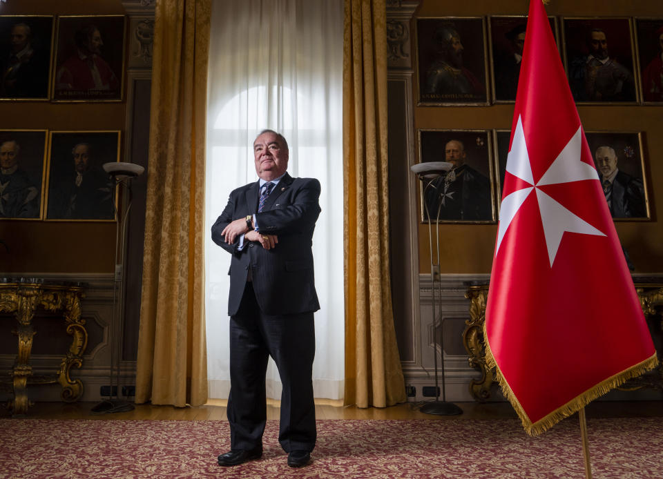 John Dunlap poses with the Sovereign Military Order of Malta's flag in the Chapter Room at their headquarters in Rome, Friday, March 31, 2023. Dunlap, a Canadian lawyer who found his vocation ministering to AIDS patients in Harlem has been elected Wednesday, May 3, 2023, the grand master of the Knights of Malta, the first non-European and first non-aristocratic head of the ancient Catholic order that provides humanitarian aid around the world. (AP Photo/Domenico Stinellis)