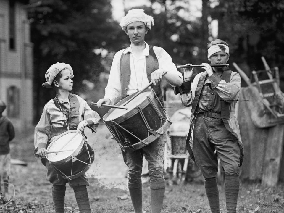 Three boys carry instruments while dressed in colonial clothing to celebrate July 4, circa 1922.