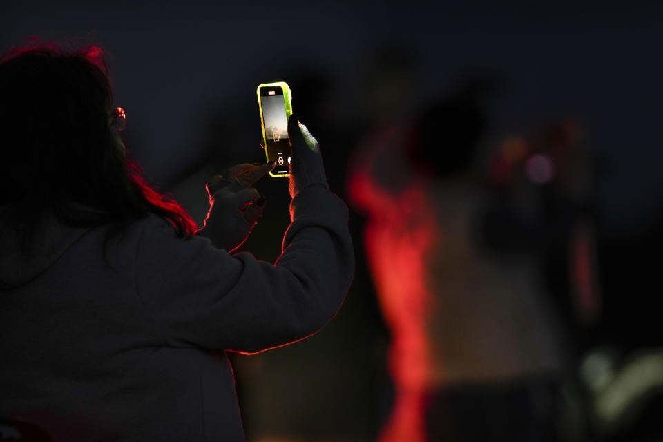 A woman records with her phone as the Mauna Loa volcano erupts Saturday, Dec. 3, 2022, near Hilo, Hawaii. (AP Photo/Gregory Bull)